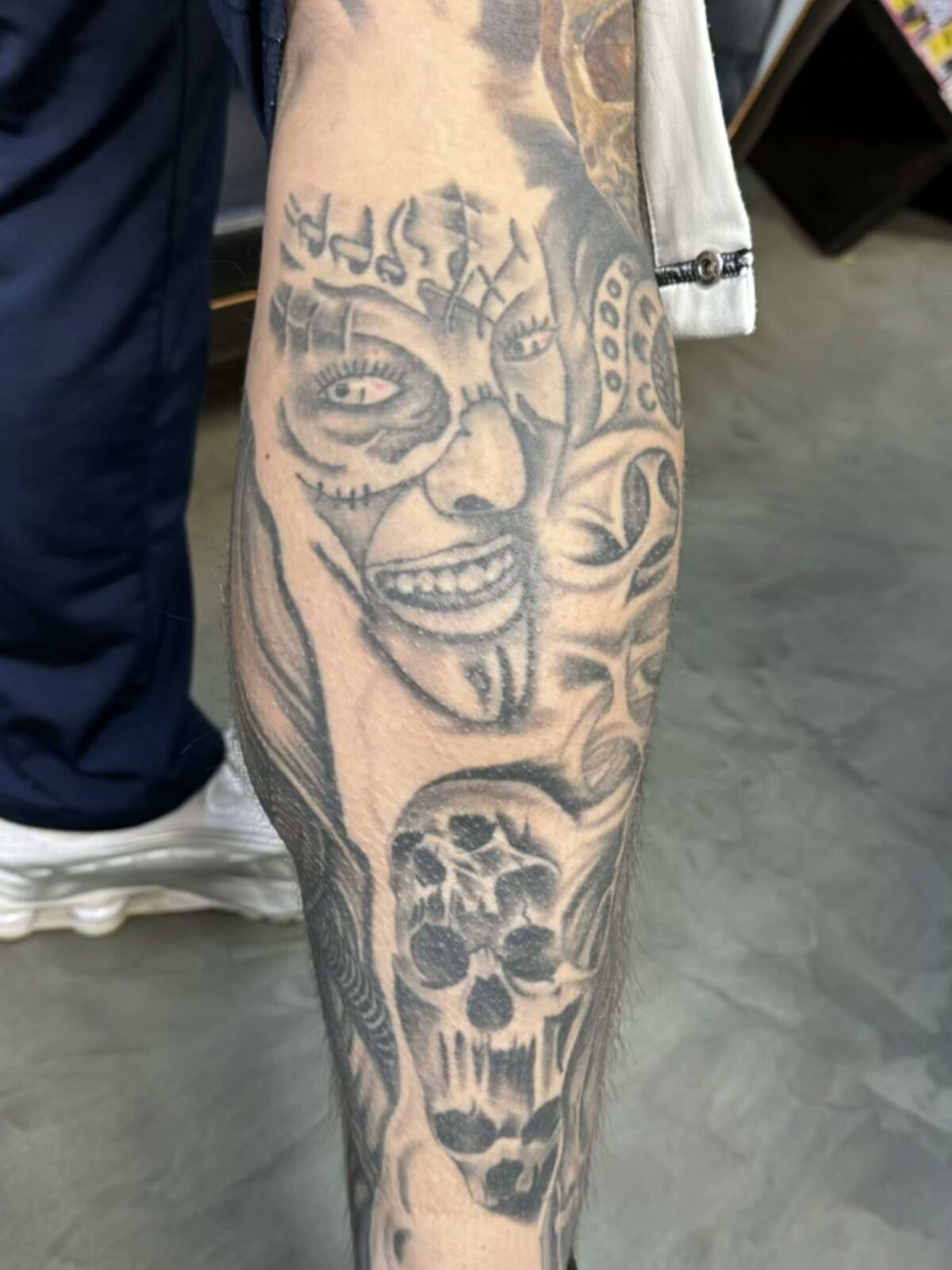 Cover-up an der Wade – Zustand vorher: altes, teilweise verblasstes schwarz-weißes Tattoo, groteskes lachendes Gesicht mit Krone, darunter ein Schädel, Breslau