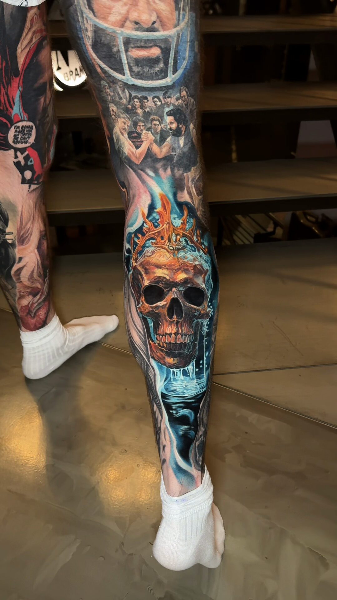 Detail des unteren Bildteils – Spiegelung des Totenkopfs im blau-türkisen Wasser, Cover-up an der Wade