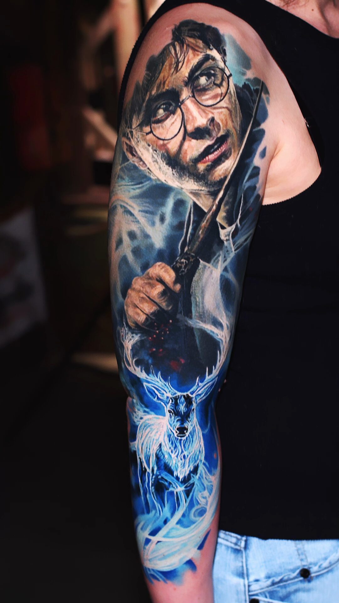 Übergang vom warmen Porträt am Oberarm zum kühlen Leuchten des Patronus – Tattoo an Oberarm und Unterarm, Wrocław