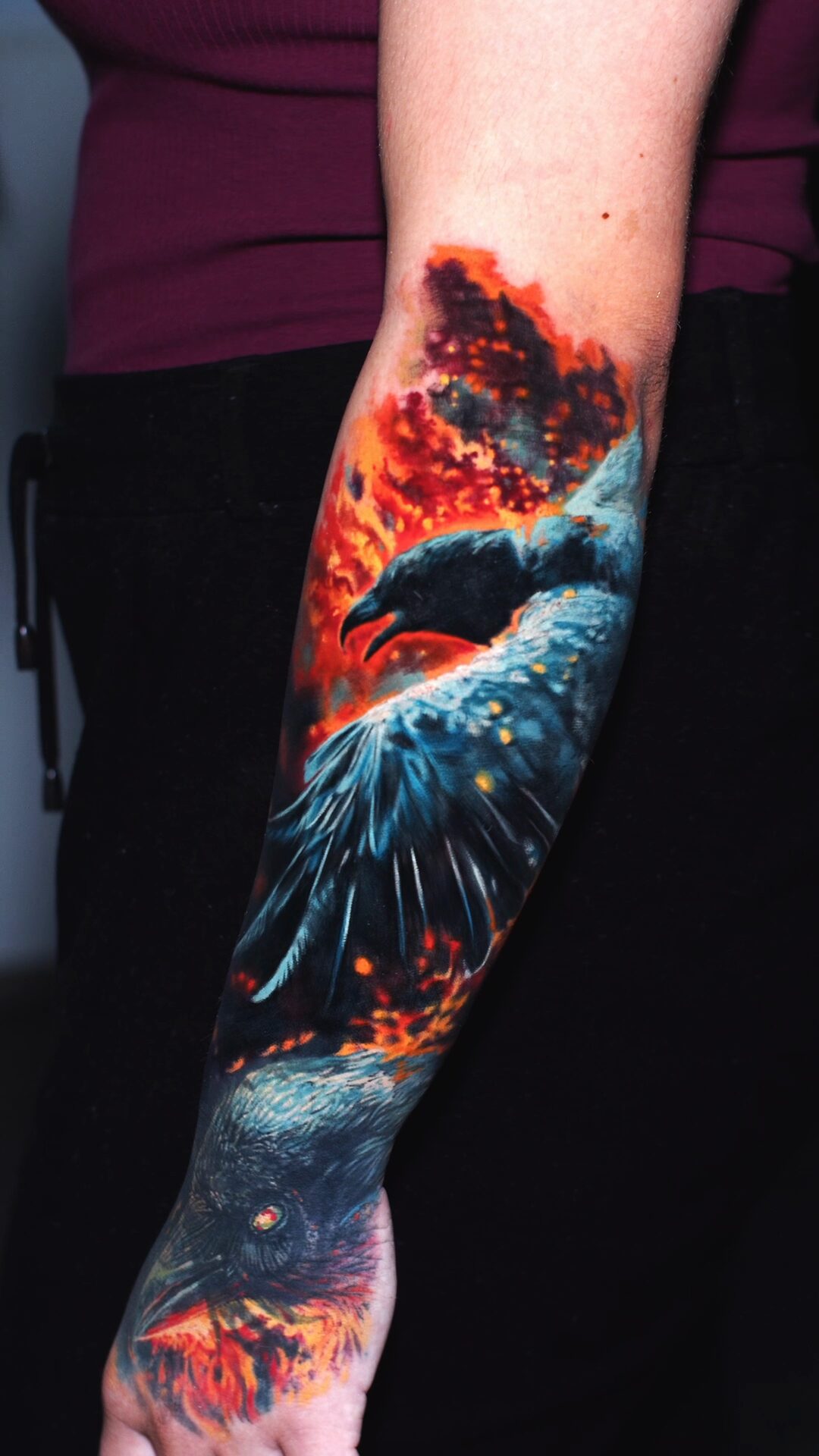 Orange-rote Flammen und Funken um den Raben – Tattoo auf dem Unterarm