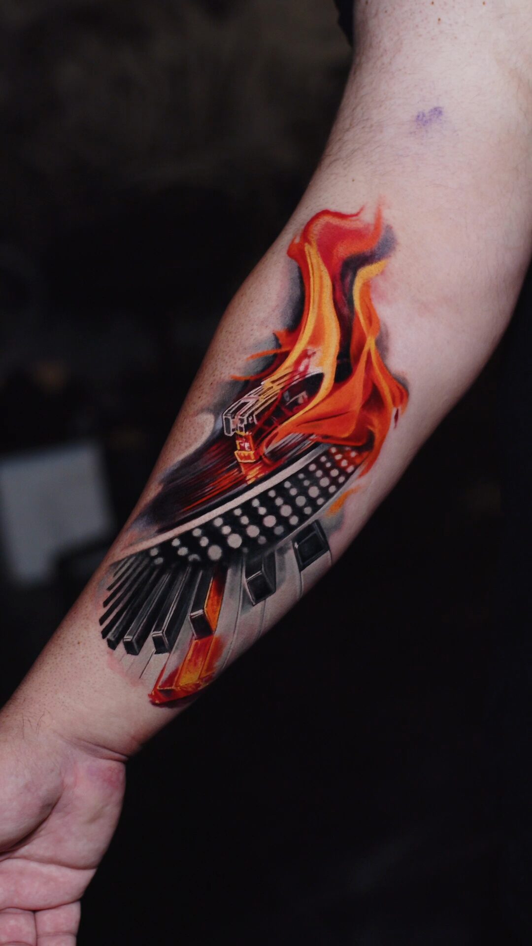Color realism tattoo by Alex666cold — a burning grand piano and Technics turntable wrapped in flames, forearm