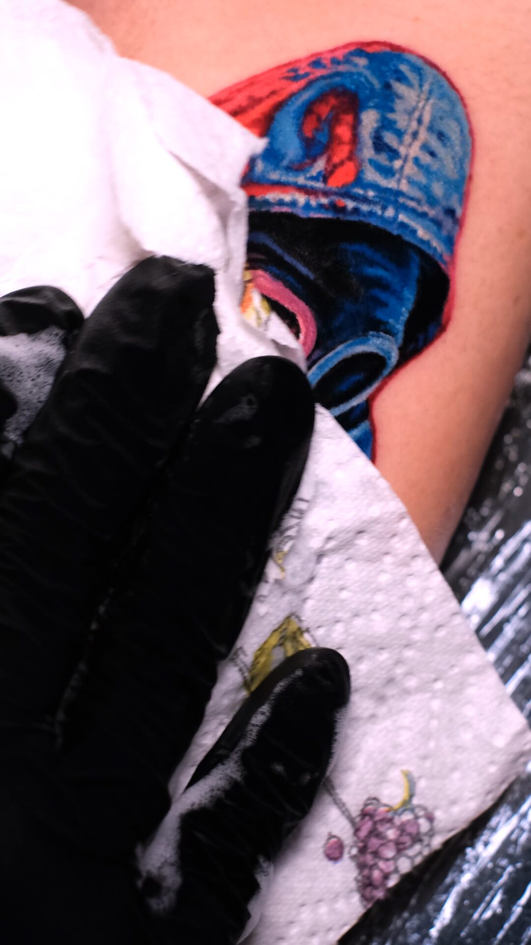 Während der Session: Handschuh und Papierhandtuch neben der Kapuze der Figur auf dem Oberarm, Tätowierer Wrocław.
