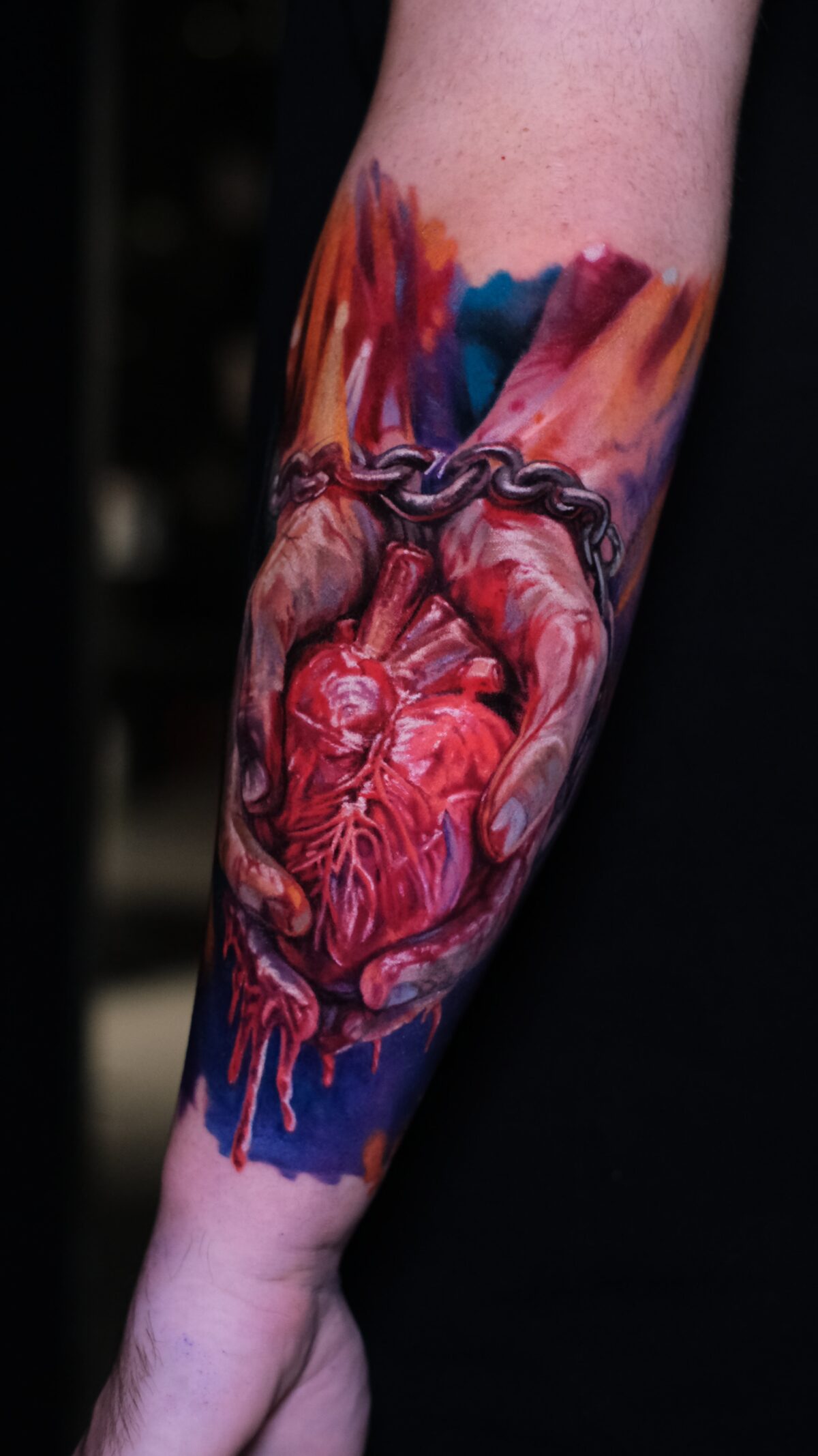 Tattoo mit Herz in Händen vor Watercolor-Hintergrund – lodernde Flammen, Orange-, Rot- und Blautöne, Wrocław