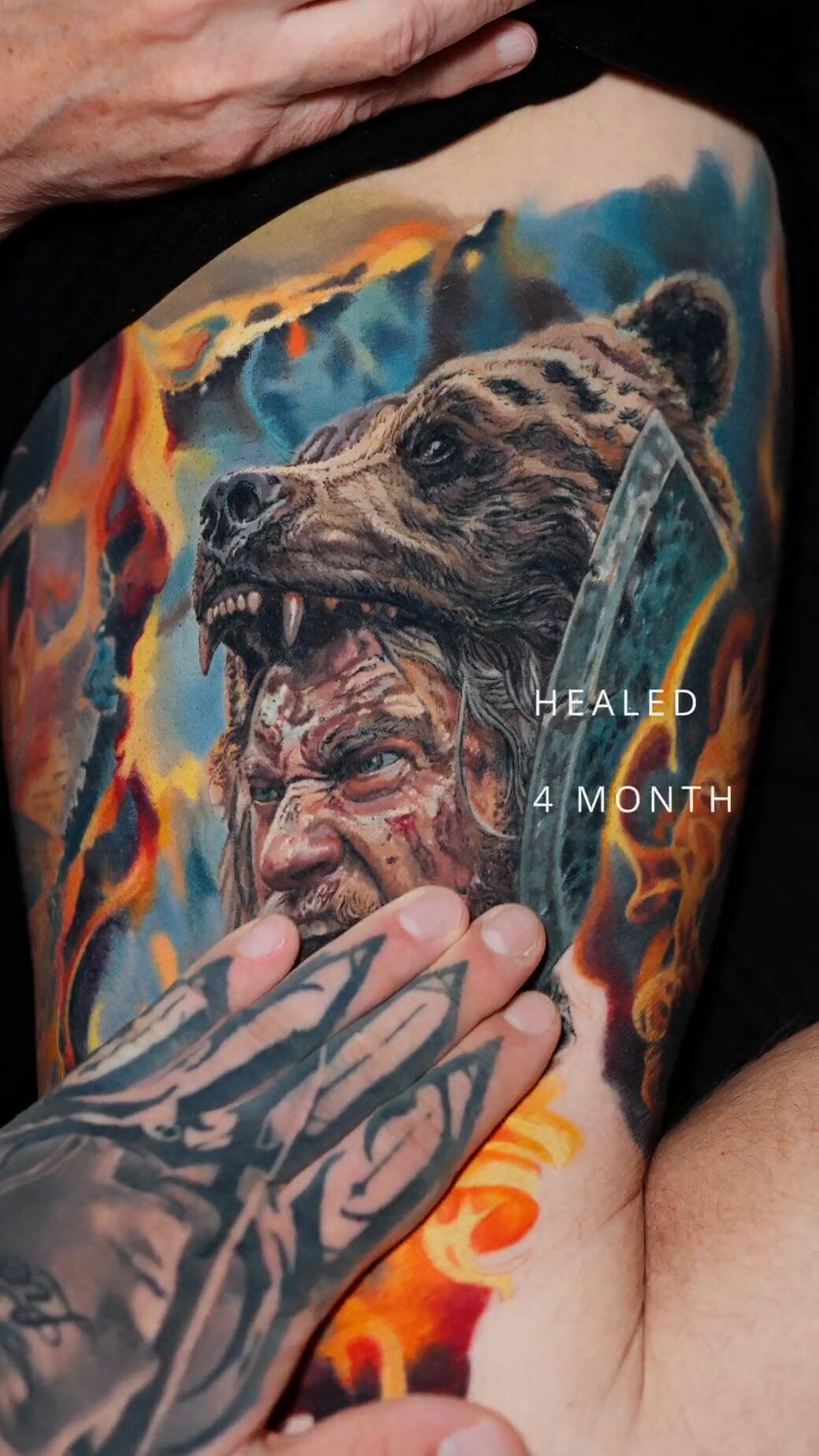 Berserker mit Bärenkopf-Kappe und Axt, Schriftzug HEALED 4 MONTH, Hand des Tätowierers verdeckt den unteren Bildrand, Wrocław.