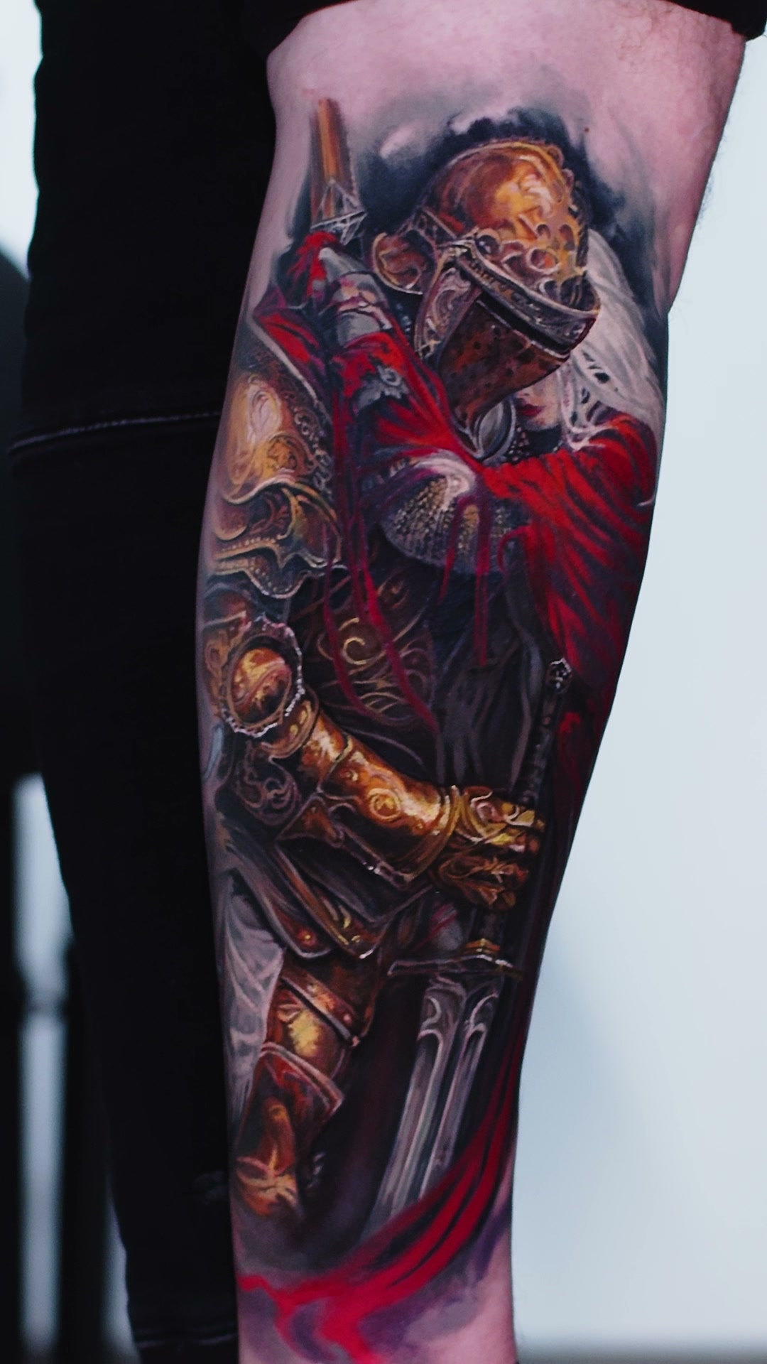 Unterer Teil des Tattoos: goldener Panzerhandschuh hält Schwert, Griff und Klinge sichtbar, unten rote Tropfen, Tätowierer Wrocław.
